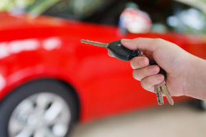 A hand activating a car key and remote with a car in the background